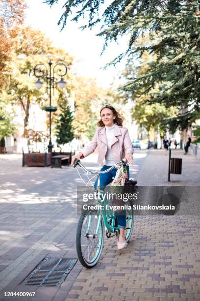 woman with mesh bag of vegetables, greenery and reusable riding a bike in the city. - biking to work stock pictures, royalty-free photos & images