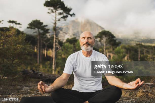 male senior practicing yoga outside with mountain view. praying and meditating alone. health and harmony with nature. - senior spirituality stock pictures, royalty-free photos & images