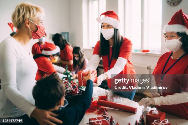weibliche freiwillige tragen gesichtsmaske geben ein weihnachtsgeschenk an einen kleinen jungen und seine mutter - chocolate pack stock-fotos und bilder