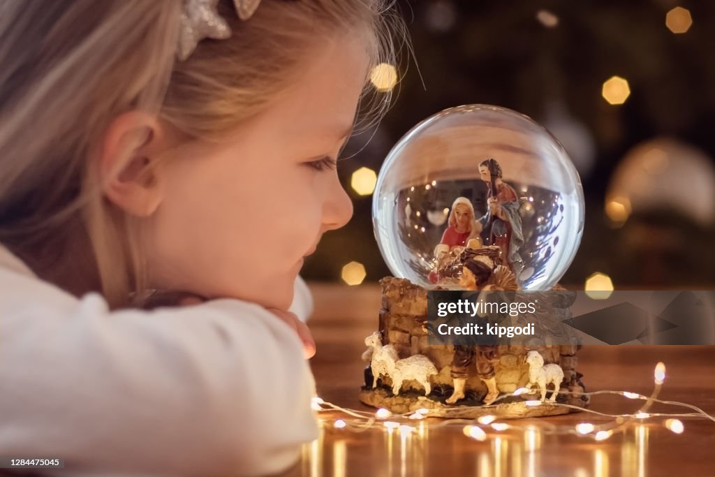 Girl looking at a glass ball with a scene of the birth of Jesus Christ in a glass ball on a Christmas tree