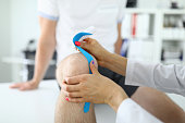 Doctor glue kinesio tape to man on his knee closeup