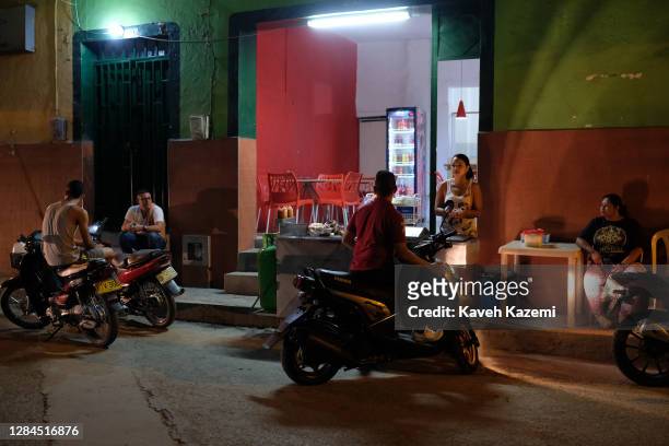 Woman stands serving food outside a fast food parlor at night while people sit in tranquility nearby on December 27, 2016 in Corinto, Colombia....