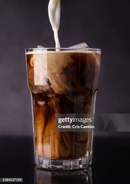 milk pouring into glass of iced coffee - coffee frappe stock-fotos und bilder