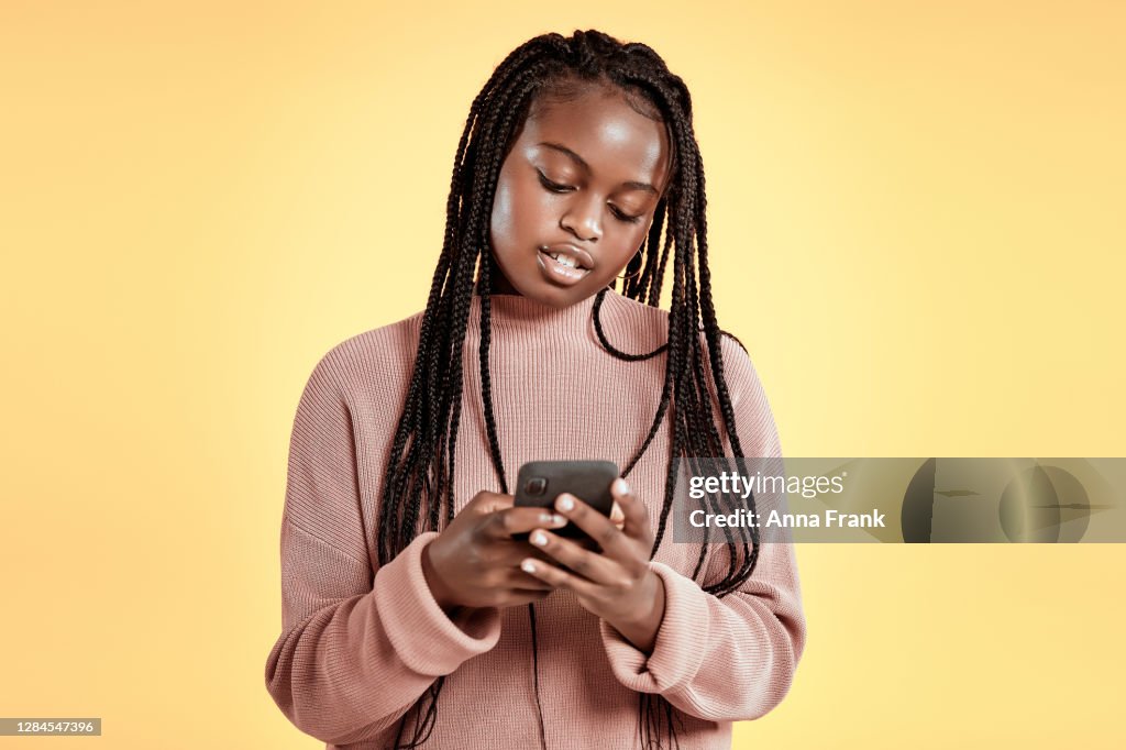 Beautiful teenager using smartphone on yellow background