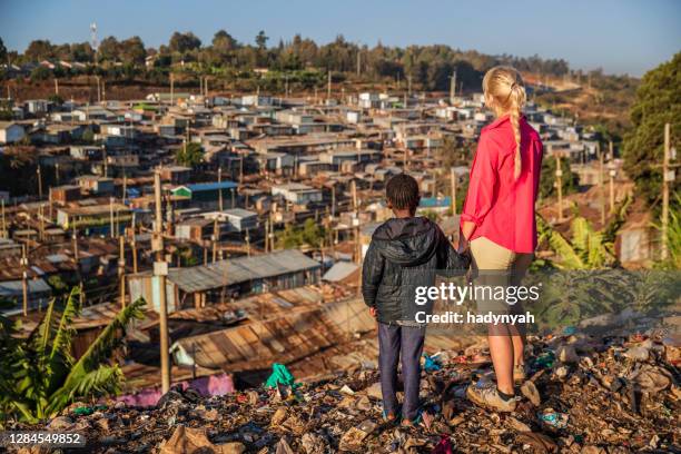 african little girl standing with young caucasian woman in trash and looking at kibera slum, kenya, east africa - slum africa stock pictures, royalty-free photos & images