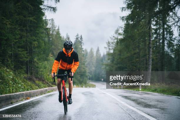 road bicyclist rides up a wet road in the rain - cycling stock pictures, royalty-free photos & images