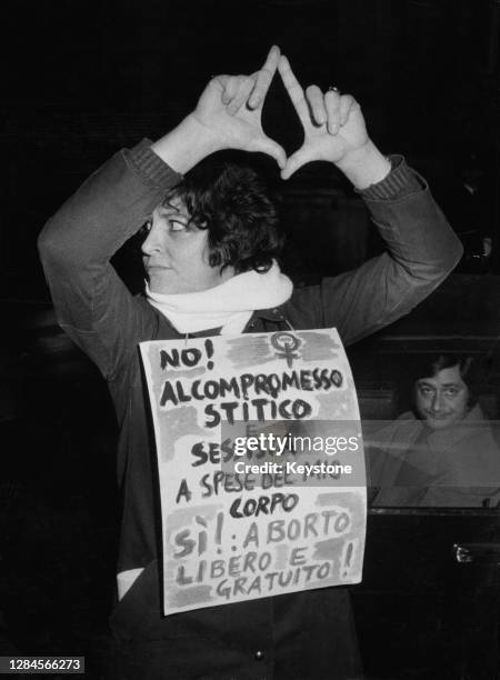 Female demonstrator makes a gesture with her hands raised above her head, wearing a placard which reads 'No! to the constipated and sexist compromise...