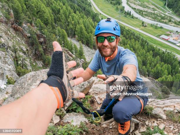 kletterer hilft teamkollegen mit helfender hand - climbing help stock-fotos und bilder