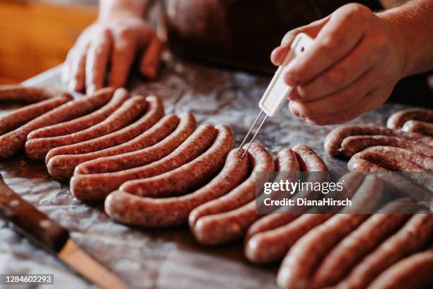 las manos masculinas pican con una aguja de carne en las salchichas con el fin de eliminar la inclusión del aire - trituradora de carne fotografías e imágenes de stock