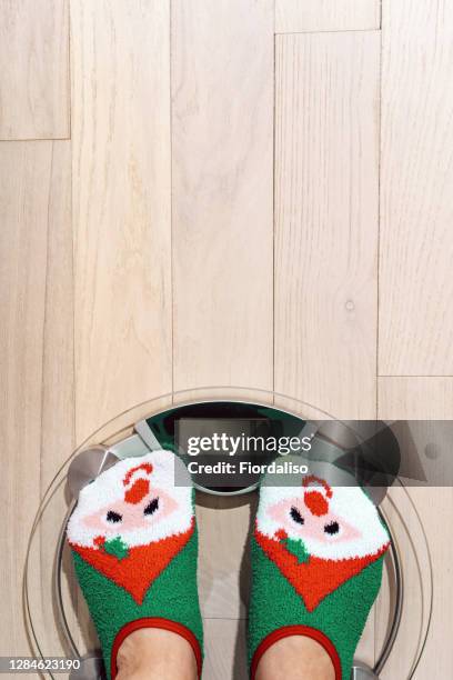 woman standing on the scales in christmas fun red green socks with snowman background. the problem of excess weight gained during the holiday new year - national diet of japan stock pictures, royalty-free photos & images