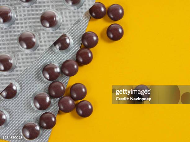 brown color medicine pills scattered on yellow background - vitamin sachet stock pictures, royalty-free photos & images