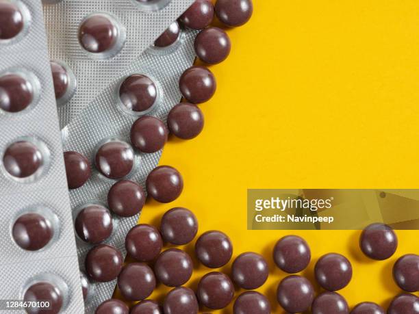 brown color medicine pills scattered on yellow background - vitamin sachet stock pictures, royalty-free photos & images