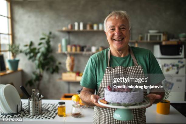 senior man holding cake that he made in kitchen at home - holding birthday cake stock pictures, royalty-free photos & images