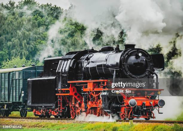 old steam train with a lot of smoke coming from the chimney driving through the countryside. - locomotive stock pictures, royalty-free photos & images