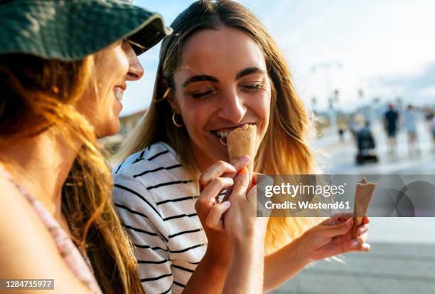 smiling young woman feeding ice cream to sister while spending enjoying in city - adult sibling stock pictures, royalty-free photos & images