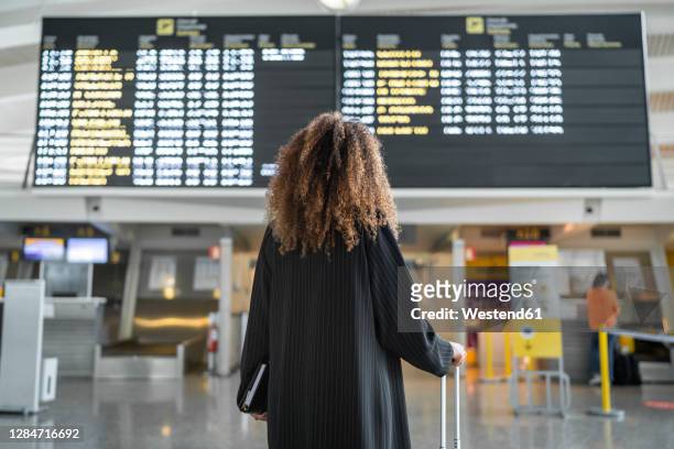 young woman checking arrival timing of flight on board standing at airport - arrival stock pictures, royalty-free photos & images