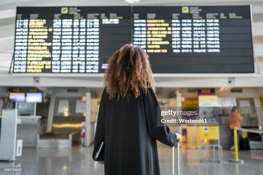 Young woman checking arrival timing of flight on board standing at airport
