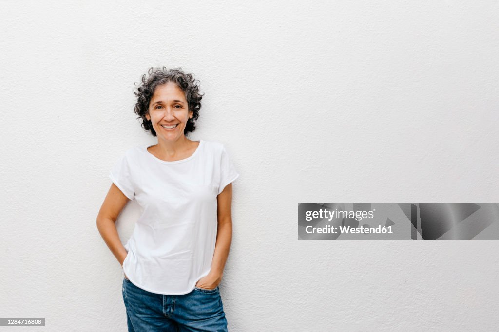 Smiling mature woman with short hair standing against white wall