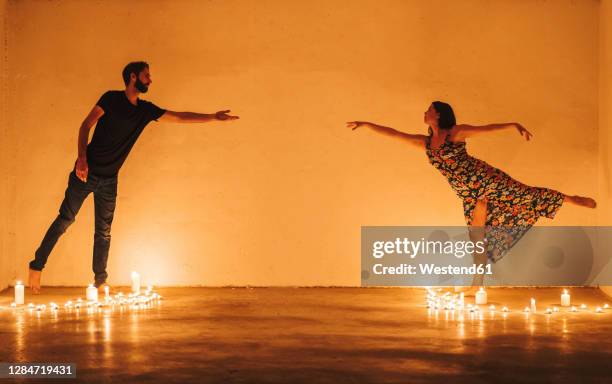 couple stretching arms to reach while standing amidst lit candles in darkroom - separation wall stock pictures, royalty-free photos & images