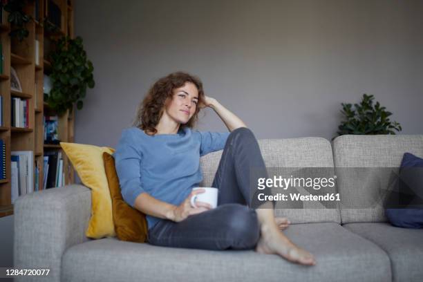 thoughtful woman with head in hands sitting on sofa at home - sofa stock-fotos und bilder