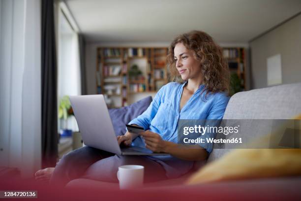 smiling woman doing online shopping on laptop at home - credit card stock pictures, royalty-free photos & images