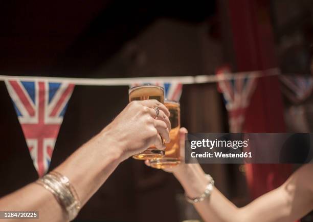 female friends toasting beer glasses while enjoying weekend at pub - british pub stock pictures, royalty-free photos & images