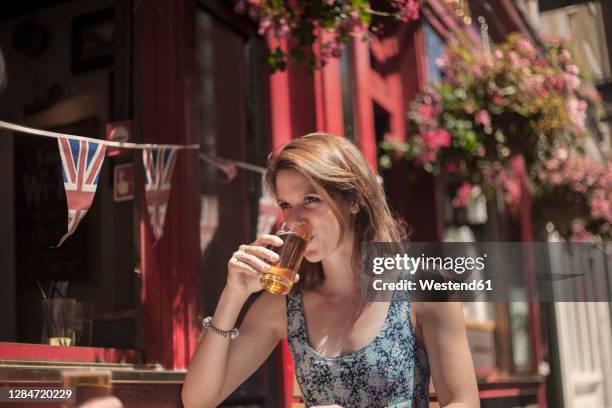 woman drinking beer while sitting outside pub during sunny day - london pub stock pictures, royalty-free photos & images