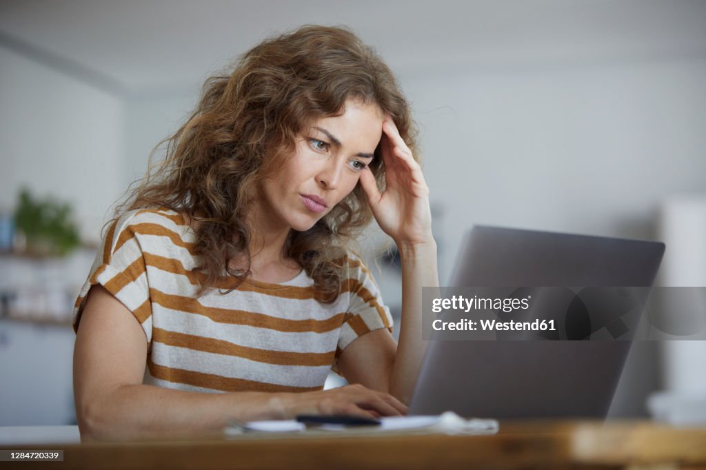 Woman sitting with head in hands while working on laptop at home