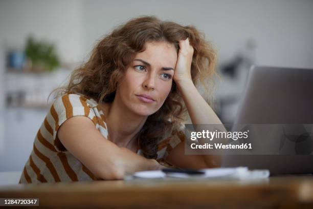 tired woman with head in hand sitting by table at home - frau stress stock-fotos und bilder