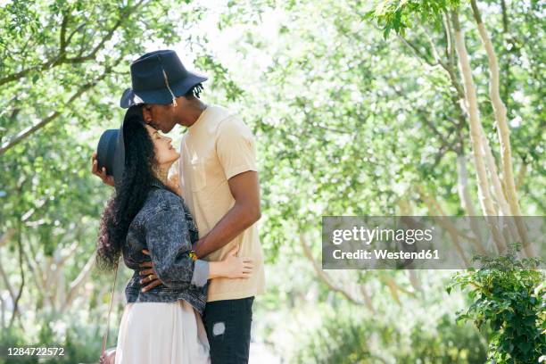 couple wearing hat kissing while standing at public park - black women kissing white men stock pictures, royalty-free photos & images