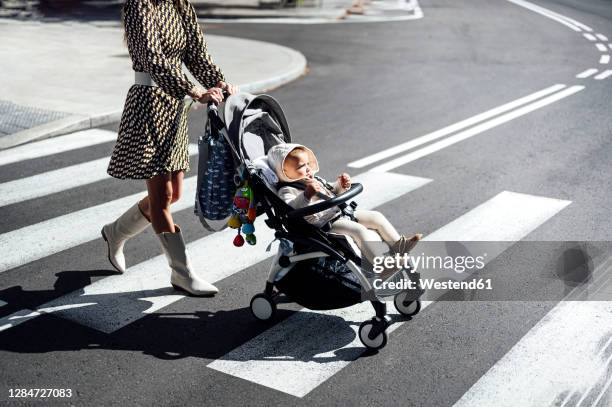 mother with baby boy in carriage crossing street in city during sunny day - cochecito de bebé fotografías e imágenes de stock