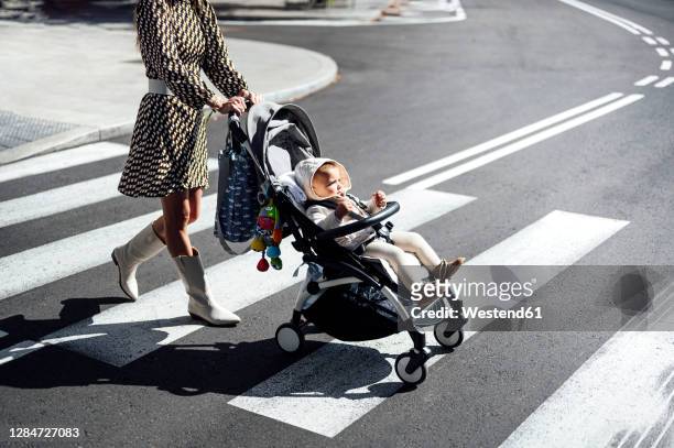 mother with baby boy in carriage crossing street in city during sunny day - 乳母車 ストックフォトと画像