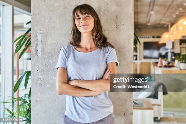 confident woman standing with arms crossed against wall at home - portrait mauer stock-fotos und bilder