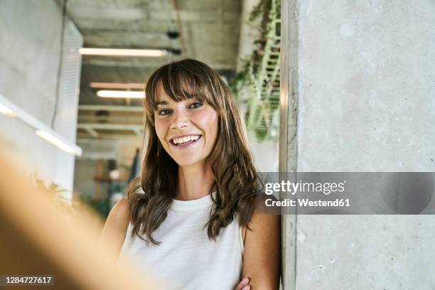 smiling woman leaning on wall while standing at home - mature brunette woman stockfoto's en -beelden