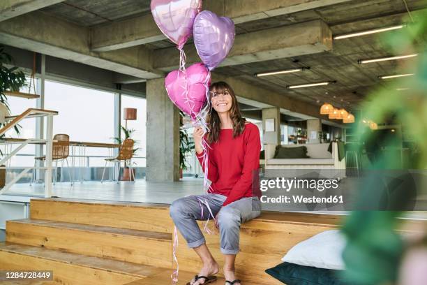 businesswoman holding balloons while sitting on stairs in loft office - work anniversary ストックフォトと画像