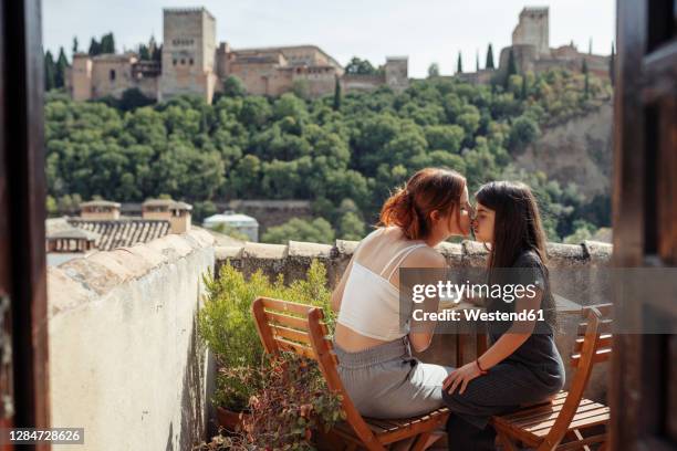 mother and daughter kissing while sitting by table on terrace - granada stock-fotos und bilder