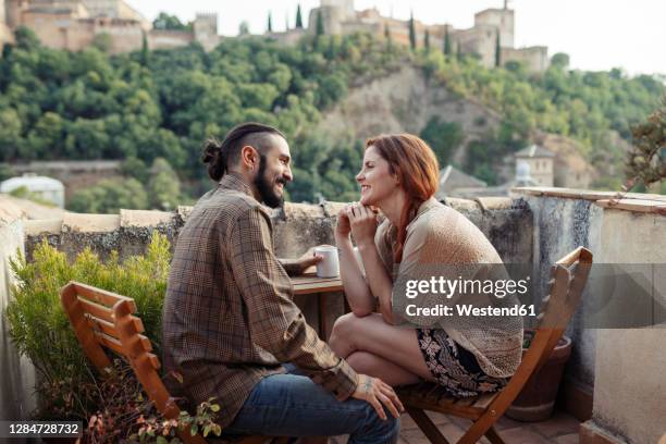 smiling couple sitting by table on roof top at home - granada spanje stockfoto's en -beelden
