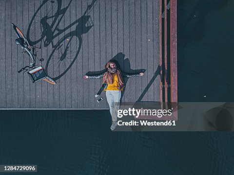 Aerial view of young woman lying on back at edge of coastal jetty Aerial view of young woman lying on back at edge of coastal jetty