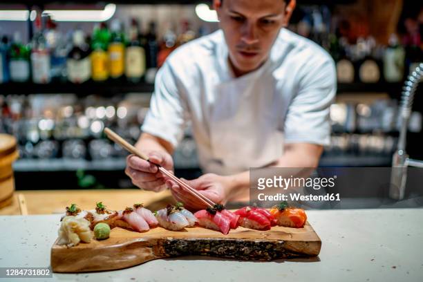 male chef garnishing sushi on wooden serving tray in kitchen at restaurant - man tray food holding stockfoto's en -beelden
