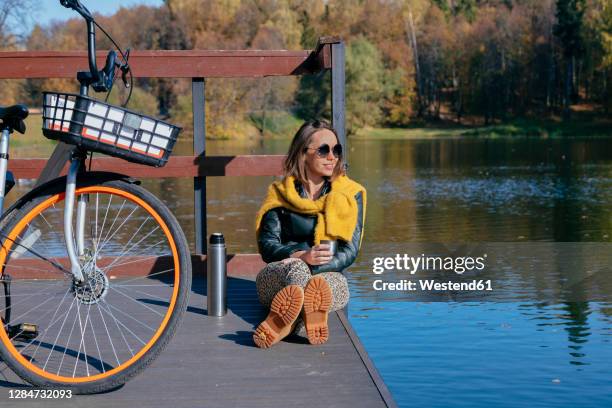 woman having coffee while relaxing on pier over lake - überkreuzte beine stock-fotos und bilder