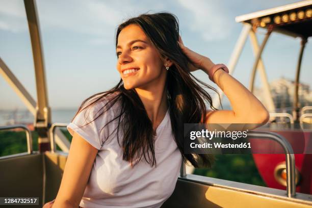 smiling beautiful young woman looking away while enjoying sunset from ferris wheel - hand in den haaren stock-fotos und bilder