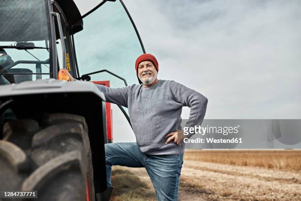 confident farmer standing with hand on hip by tractor at farm - hand on hip stock pictures, royalty-free photos & images