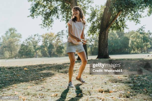 mature woman throwing frisbee ring while standing in public park on sunny day - frisbee fotografías e imágenes de stock