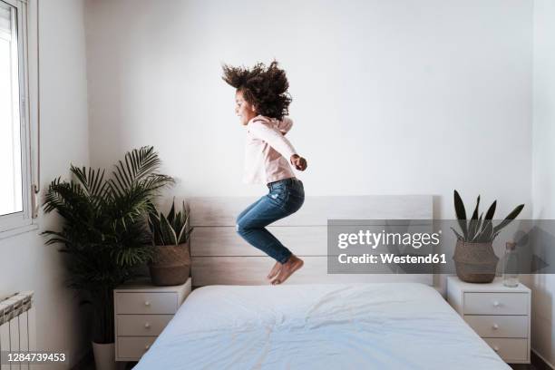 cute girl jumping on bed in bedroom at home - jump on bed photos et images de collection