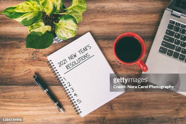 2021 new year's resolutions text written on notepad with laptop and cup of coffee on top of wooden desk - january background stock-fotos und bilder