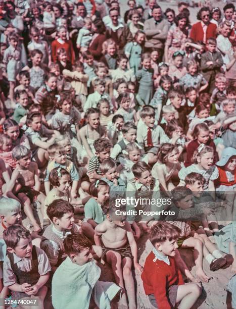 Young children on holiday sit on the sand to watch a Punch and Judy puppet show on the beach at the seaside resort of Broadstairs in Kent, England in...