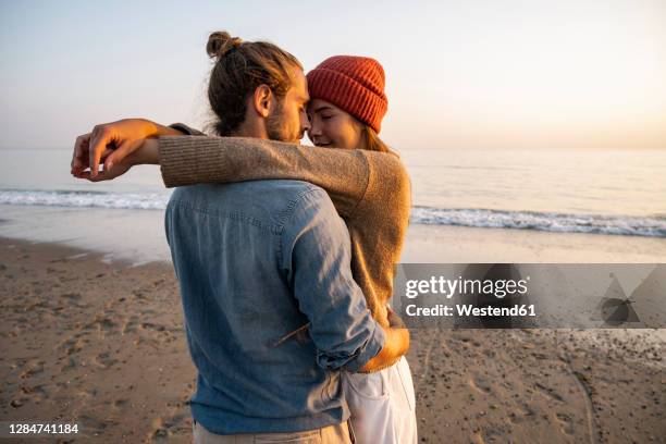 young romantic couple standing face to face at beach against clear sky during sunset - couples romance stock pictures, royalty-free photos & images