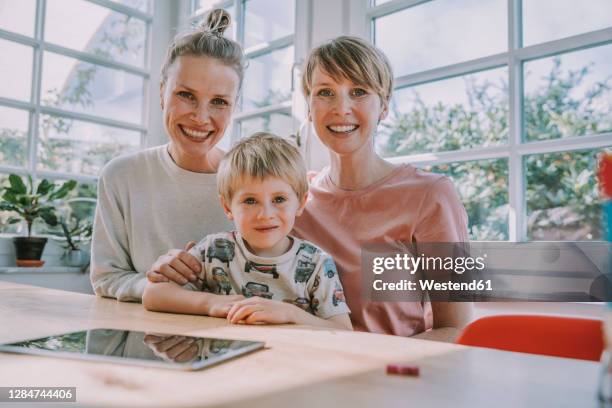 smiling mothers sitting with son at home - lesbica foto e immagini stock