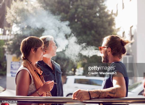 friends smoking while standing outdoors on sunny day - smoke stock-fotos und bilder