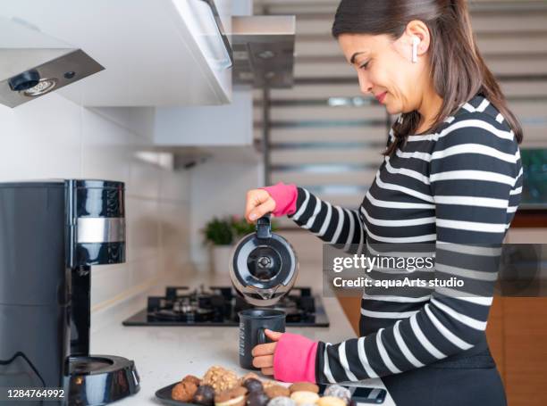 de aantrekkelijke jonge glimlachende vrouw heeft het gesprek van de werkconferentie met slimme telefoon van huisbureau terwijl het voorbereiden maak koffie - koffiepot stockfoto's en -beelden